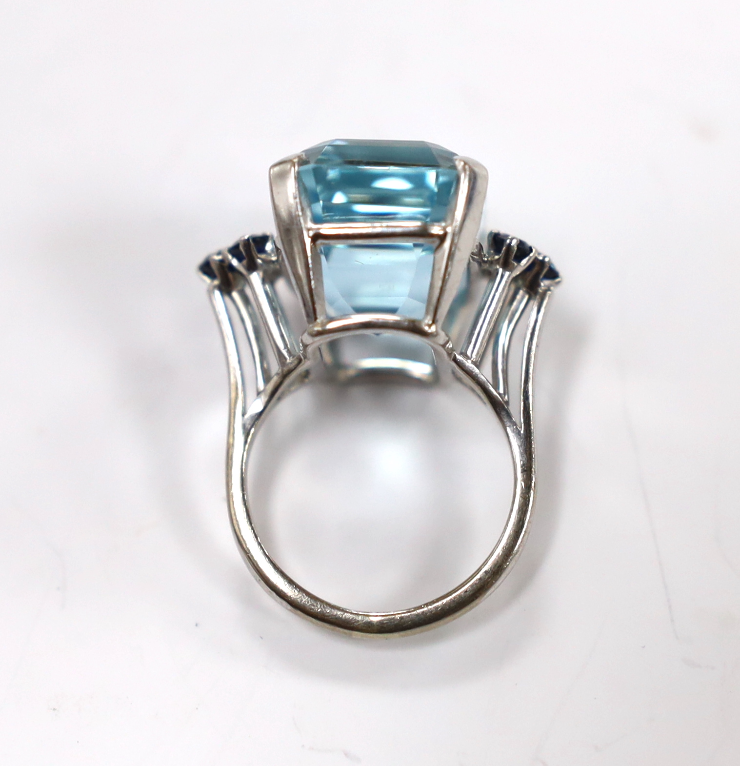 An 18ct white metal and single stone emerald cut aquamarines set dress ring, with six stone sapphire set shoulders, size L, gross weight 11.7 grams.
